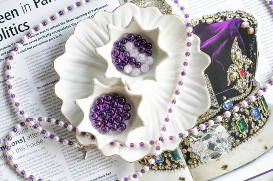 Amethyst beads in a decorative dish with purple jewelry displayed on magazine background.