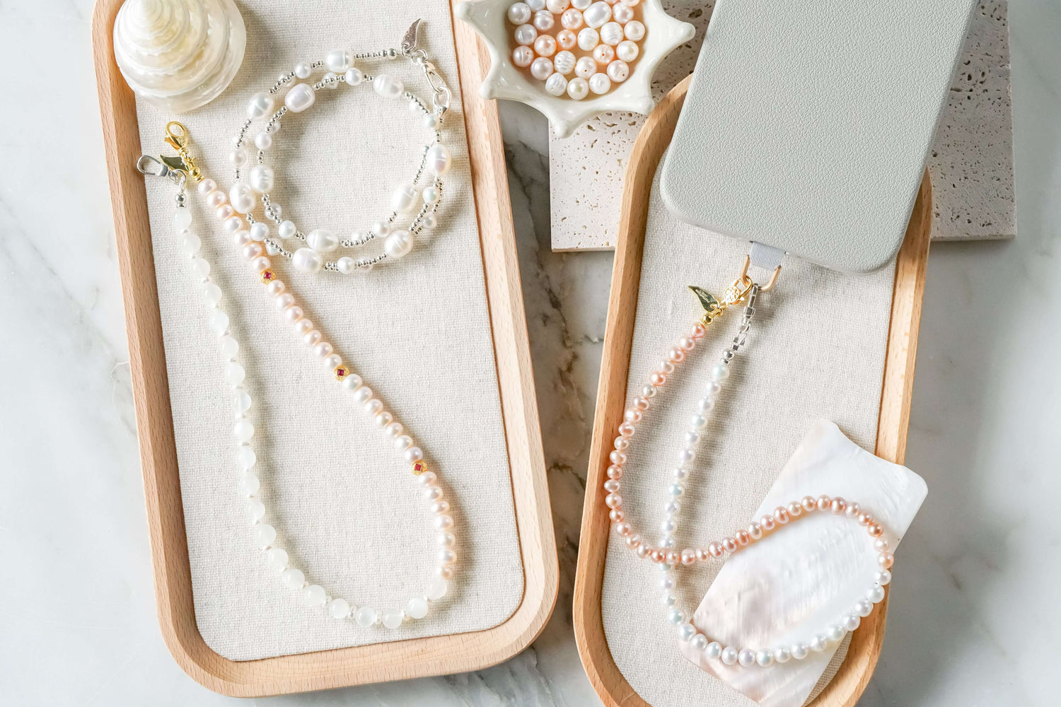 Elegant jewel phone charms and bracelets displayed on a wooden tray with pearl accents.