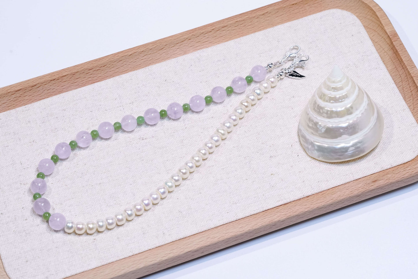 Pearl-lavender amethyst-nephrite jade phone charm bracelet on display with a seashell on a wooden tray.